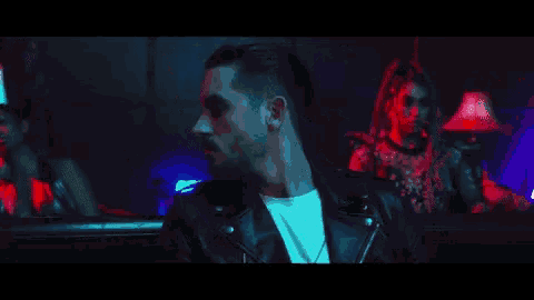 a man in a leather jacket is sitting in a dark room with two women .