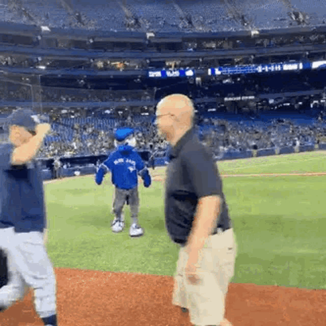 a man and a boy are standing on a baseball field . the boy is wearing a blue jays jersey .