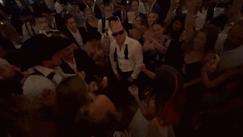 a man wearing sunglasses stands in the middle of a crowd of people at a party