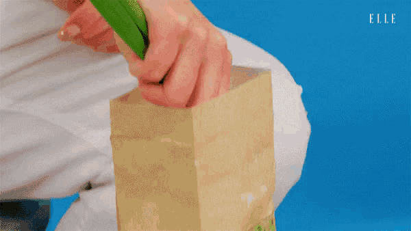 a person is opening a brown paper bag with a green item in it .