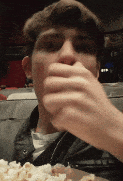 a man covering his mouth with his hand while eating popcorn in a theater