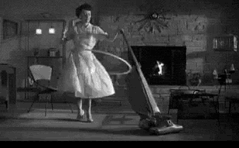 a woman in a white dress is dancing in a living room while holding a vacuum cleaner .