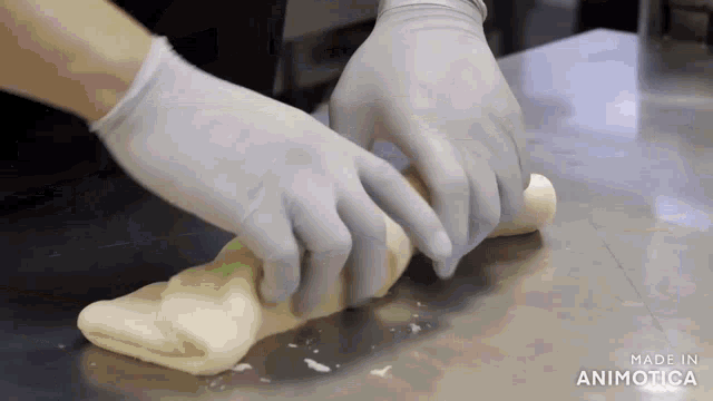 a person wearing gloves is rolling dough on a table .