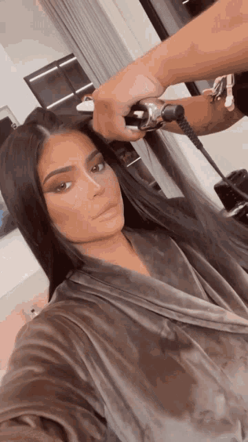 a woman in a robe is getting her hair straightened by a man