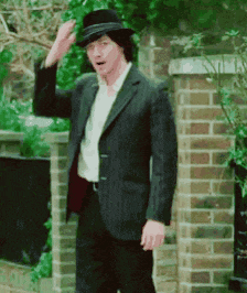 a man in a suit and hat standing in front of a brick wall