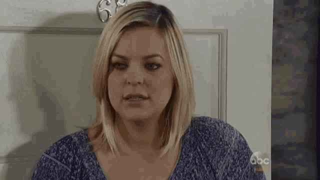 a woman in a purple shirt is standing in front of a door and making a funny face .