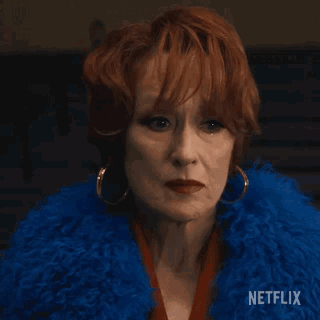an older woman with red hair is wearing a blue fur coat and earrings .