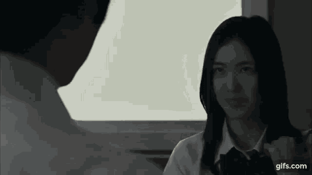 a man and a woman are looking at each other in a dark room . the woman is wearing a school uniform .
