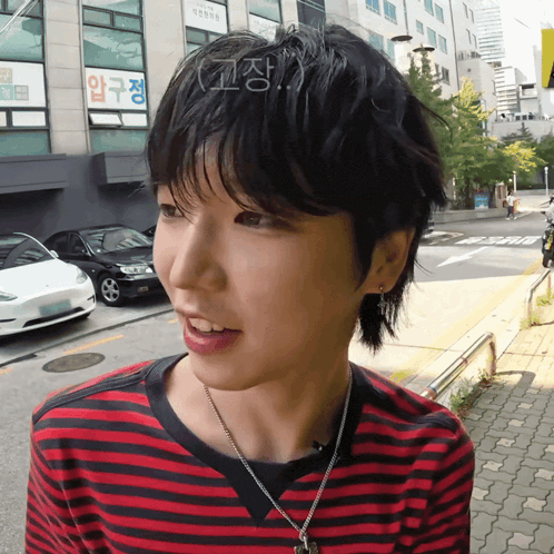 a woman wearing a red and black striped shirt is standing on a street