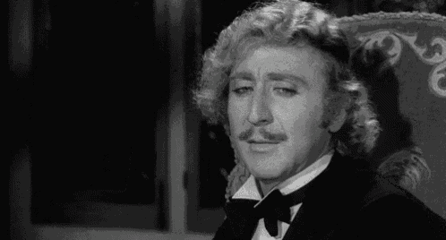 a black and white photo of a man in a tuxedo sitting in a chair .