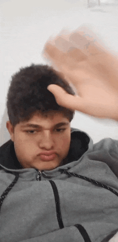 a young man in a grey hoodie is making a funny face while holding his hand to his head .