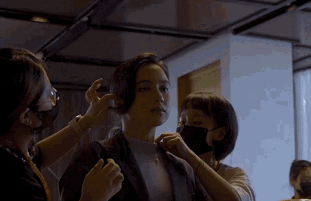 a woman is getting her hair done by two women wearing masks