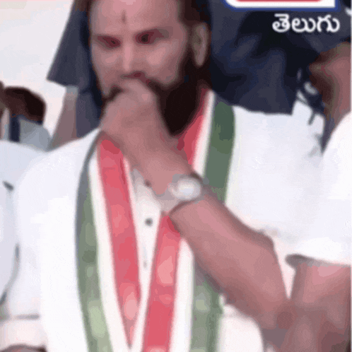 a man with a beard is wearing a white shirt with a green and red sash around his neck