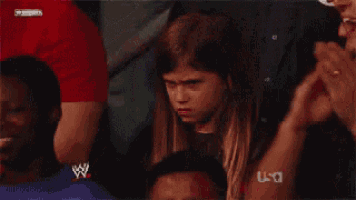a young girl is sitting in a wrestling ring with a man in a usa shirt behind her .