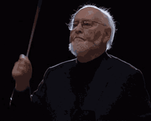 a man with a beard and glasses is holding a conductor 's baton