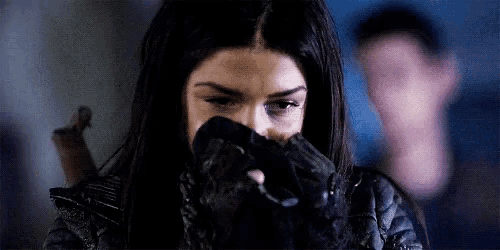 a woman is covering her face with a black glove while a man is standing in the background .