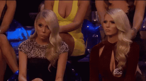 two blonde women are sitting next to each other in a crowd of women .