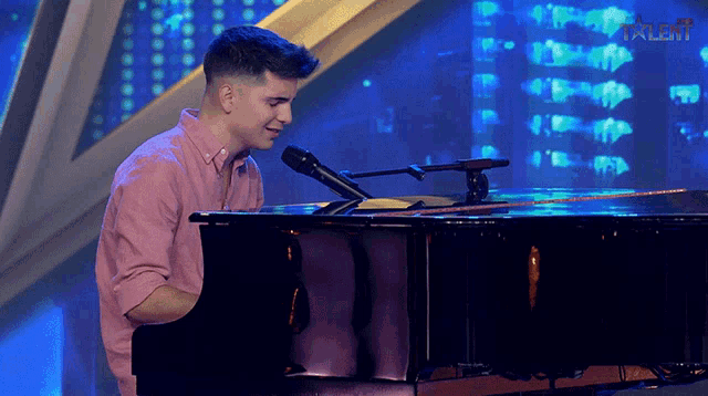 a man in a pink shirt is playing a piano and singing into a microphone in front of a talent logo