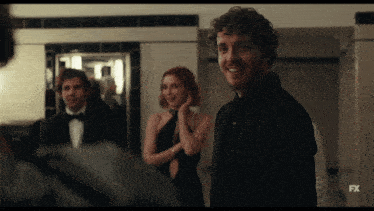 a man in a black suit is smiling in front of a tv screen that says fx on it