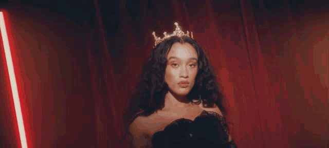a woman wearing a tiara and black gloves stands in front of a red curtain