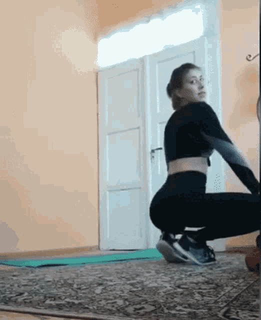 a woman is squatting on a yoga mat in front of a mirror in a living room .