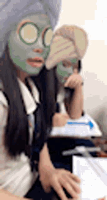 a woman with a cucumber mask on her face is sitting next to another woman with a mask on her face .