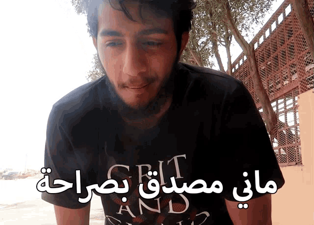 a man with a beard wears a shirt that says grit and sand