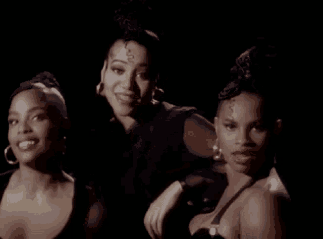 a group of three women are standing next to each other in a dark room and singing .