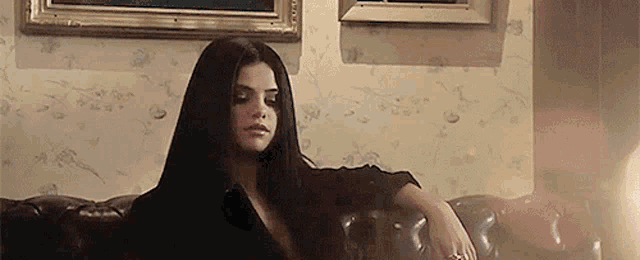 a woman is sitting on a couch in a living room with a painting on the wall behind her .