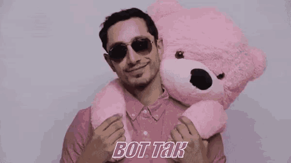 a man wearing sunglasses is laying on a bed with a pink background .