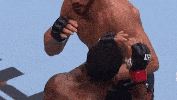 a man wearing a pair of ufc gloves is fighting another man on a blue surface .