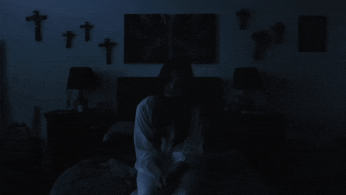 a woman sits on a bed in the dark