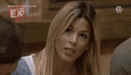a woman is sitting at a table with her hand on her chin and looking at the camera .