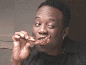 a man in a black shirt is eating a piece of meat with his eyes closed