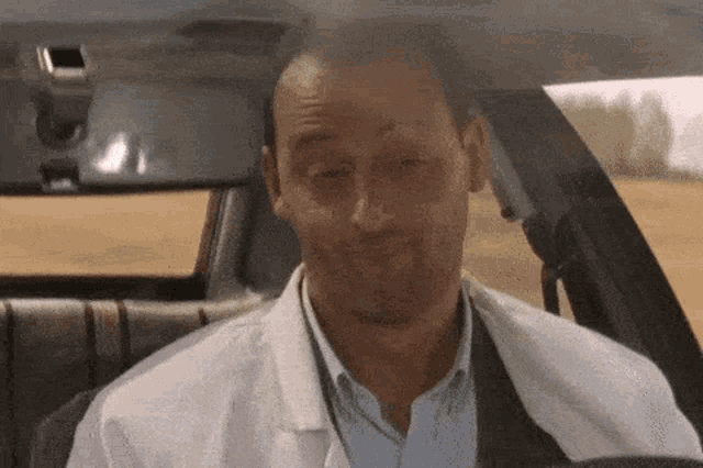 a man in a lab coat is sitting in the back seat of a car making a funny face .