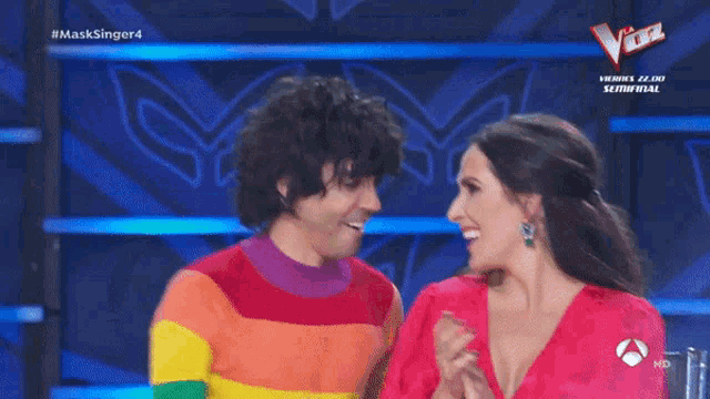 a man in a rainbow sweater and a woman in a red dress are on a tv show called masksinger4