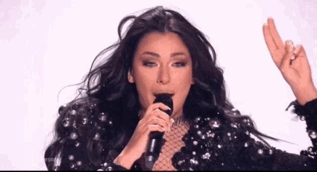 a woman singing into a microphone with her arms outstretched
