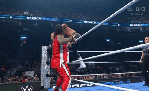 a wrestler in a red jersey is standing in a boxing ring .