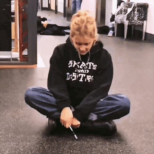 a person wearing a black hoodie that says skate on it sits on the floor