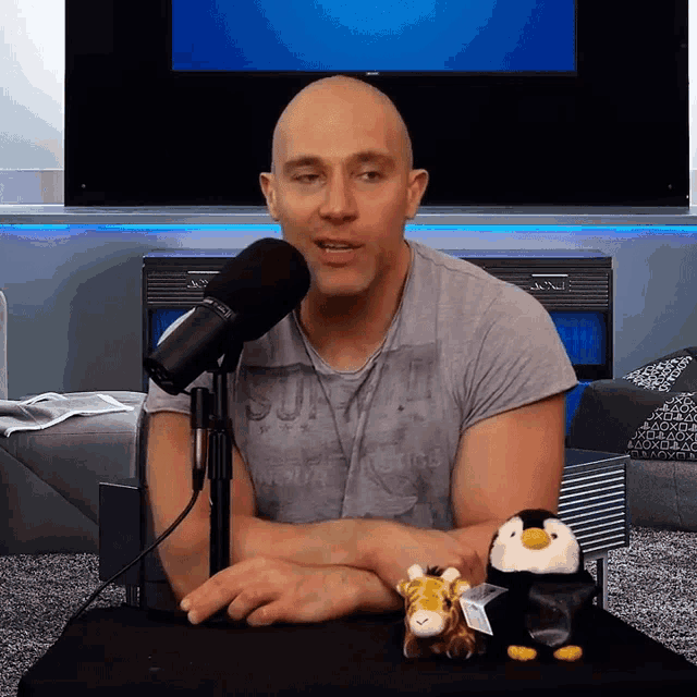 a bald man is sitting in front of a microphone wearing a shirt that says superdry