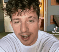 a man with curly hair and a beard is wearing a white t-shirt and smiling .