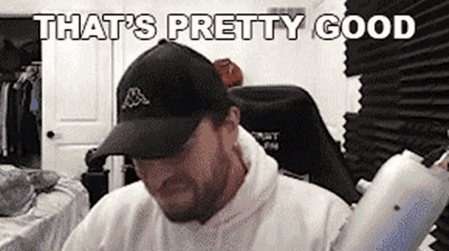 a man wearing a black hat and a white hoodie is sitting in a chair in a room .