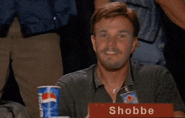 a man is sitting at a table with a sign that says shobbe on it