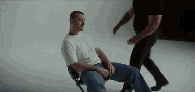 a man is sitting in a chair while another man stands behind him