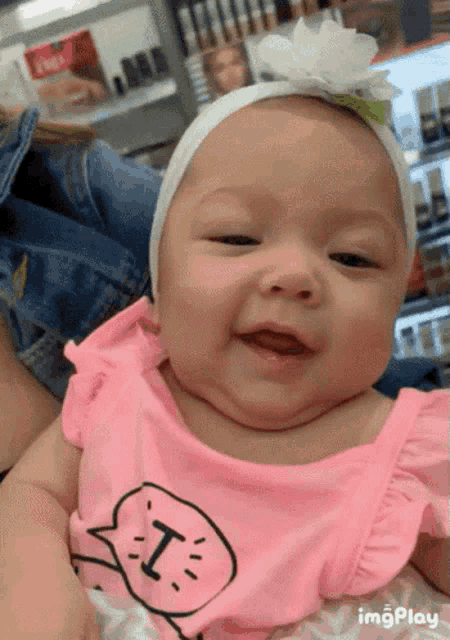 a baby wearing a pink shirt with the letter t on it is smiling
