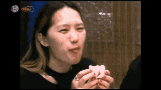 a woman is eating a piece of food with a s on the bottom right