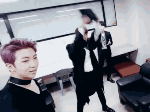 a man with purple hair is standing in a room with two other men .