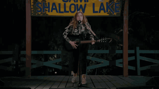 a girl singing into a microphone while playing a guitar under a sign that says shallow lake