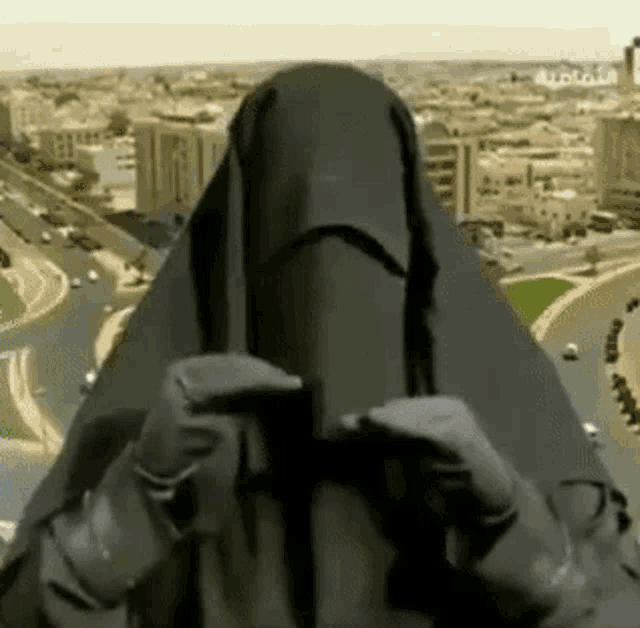 a woman wearing a black veil is standing in front of a cityscape
