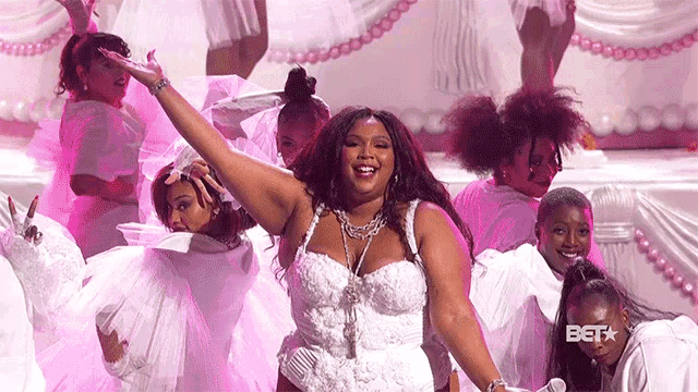a woman in a white dress is standing on a stage with a group of women in pink dresses .